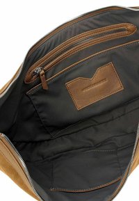 Interno di una borsa in suede beige con fodera in tessuto nero, una tasca con zip, una tasca piatta e un dettaglio di etichetta in pelle marrone cucito.