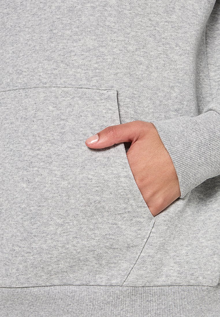 Sudadera gris con un bolsillo canguro frontal. Hecha de una tela suave con un acabado texturizado y puños de canalé. Costuras detalladas visibles.