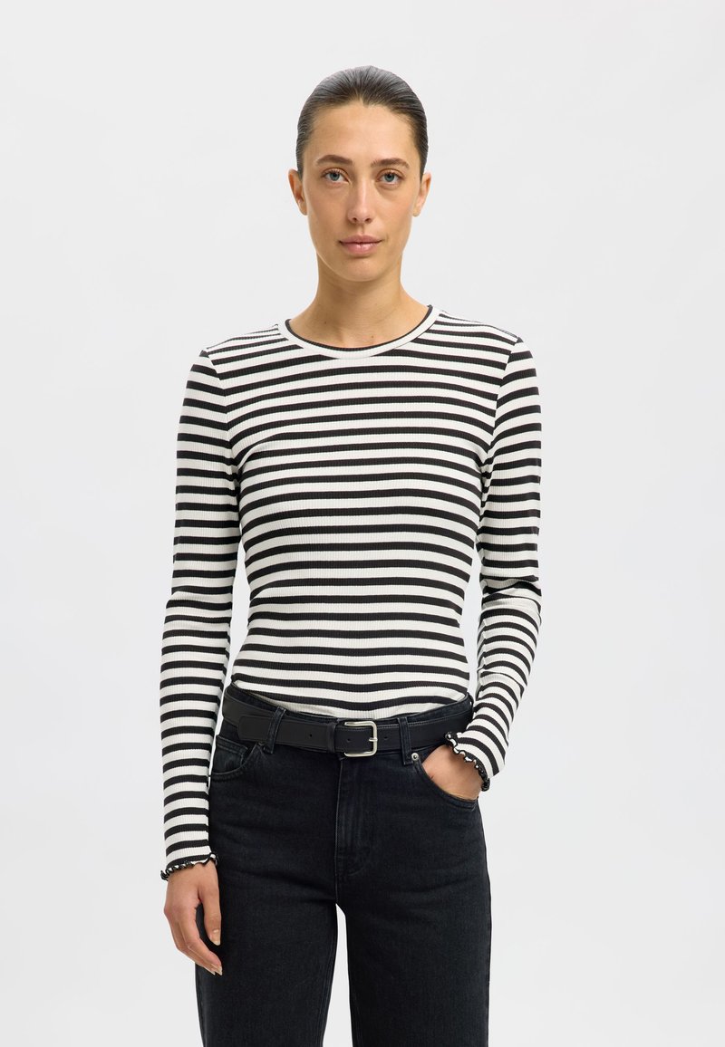 Svart-hvitt stripete langermet skjorte med ribbet tekstur og rund hals, kombinert med høy midje svarte jeans og et svart belte.