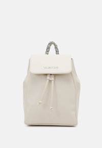 Beige Valentino ryggsäck med dragsko, klaff med logotyp och silverfärgad kedja som handtag, visad mot en vit bakgrund.