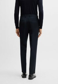Mörkblå skräddarsydda byxor med en slät struktur, smal passform och två bakfickor med knappstängning, som matchas med svarta skor.