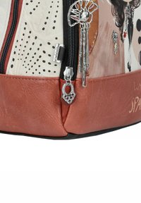 Sac en cuir marron avec un dessus texturé crème, orné de pois et de charm's décoratifs. Comprend une fermeture éclair en métal et un art graphique distinct.