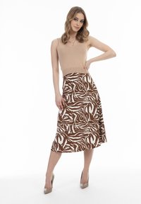 Yksivärinen beige toppi yhdistettynä ruskeaan midihameeseen, jossa on valkoinen abstrakti seepra-kuvio, päällä beige korkokengät valkoisella taustalla.