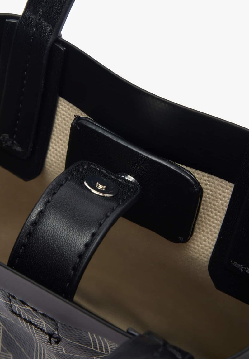Poignées en cuir noir avec un bouton-pression en argent, contrastant avec un intérieur beige, mettant en valeur un motif texturé le long du bord du sac.