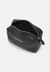 Černá kožená taška s texturou, zlatým kováním, zipovým uzávěrem a vnitřními přihrádkami. Na přední straně se nachází logo "VALENTINO" ve zlaté barvě.