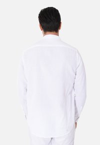 Camicia bianca a maniche lunghe in lino, con colletto button-down e orlo curvo, mostrata dal retro senza pattern visibili.