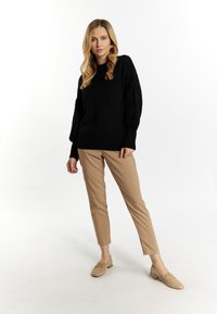 Černý pletený svetr s texturovanými rukávy, hnědé upravené kalhoty a béžové mokasíny. Představuje přiléhavý siluet s casual stylem.