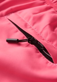 Heldere roze stof met een ritszak en zwarte hardware, inclusief een logo-treklip en contrasterende naadstiksels.