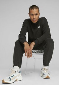 Top sportivo nero con zip a quarti e logo bianco, abbinato a pantaloni jogger coordinati e sneakers bianche con dettagli in turchese e beige.