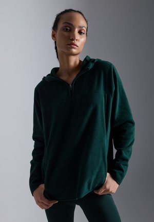 Zeleni flis pulover s polu-zip ovratom, dugim rukavima i opuštenim krojem. Mekana tekstura s glatkom završnom obradom.