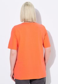 Camiseta de manga corta naranja con escote redondo. La tela parece suave, con un corte relajado y un dobladillo recto a la altura de la cintura.