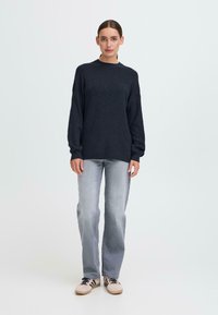 Námornická pletená svetr s ribbed texturou, kulatým výstřihem a spuštěnými rameny, doplněný o světle šedé džíny a béžové tenisky.