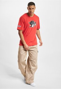 Rød bomulls t-skjorte med en svart og hvit grafisk logo, kombinert med beige cargo-bukser. Buksemodellene har flere lommer og en løs passform.