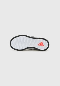 Semelle de chaussure de sport noire avec une surface en caoutchouc blanc texturé, présentant un motif hexagonal et le logo Adidas rouge. Design non-marquant.