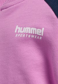 Sweatshirt de sport rose avec des accents bleu marine, présentant une texture côtelée et un logo "hummel SPORTSWEAR" en blanc bien visible à l'avant.