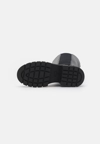 Schwarze Schuhsohle mit einem strukturierten Profil. Das Material wirkt gummiartig, mit einer runden Spitze und einem strukturierten Design.
