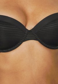 Black strapless bikini top with ribbed texture, featuring a smooth finish and curved edges, designed for support and style.