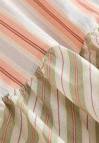 Détail du tissu montrant une couture froncée joignant des panneaux de coton à rayures verticales pêche et vert.