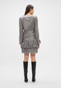 Hõbedane sädelev kleit pikkade varrukatega, volangiga vöökoht ja kihiline volangäär; ühendatud põlvekõrguste mustade saapatega.