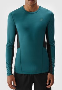 Camiseta deportiva de manga larga en azul verdoso con paneles laterales negros, hecha de una tela liviana y elástica. Presenta un escote redondo y un diseño ajustado.