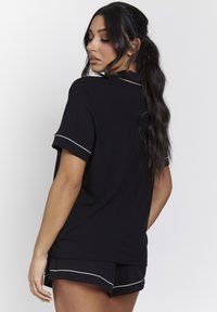 Zwart loungewear-set bestaande uit een ribbelhoogte top met korte mouwen en bijpassende shorts, afgewerkt met witte bies langs de randen.