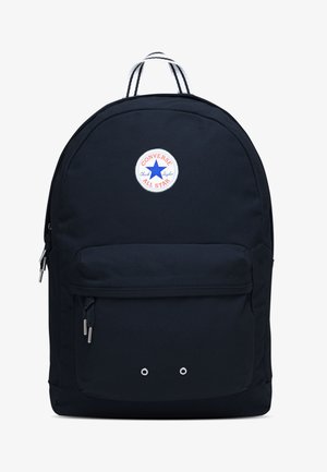 Sac à dos noir avec une patch ronde blanche arborant une étoile bleue et un texte rouge. Deux poches zippées à l'avant et des détails en métal gris. Tissu texturé.