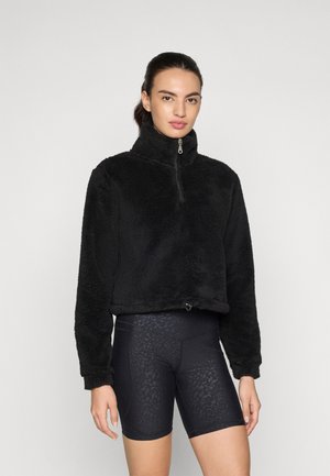 Svart fleece cropped genser med høy krage og halv glidelås, paired med svarte sykkelshorts med et subtilt dyremønster.