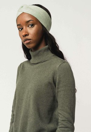 Gebreide groene haarband met een geknoopte detail bovenop; gedragen met een bijpassende groene coltrui. Soepele textuur, aangesloten ontwerp.