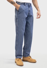 Blue denim jeans with a straight-leg design, featuring side pockets and a faded texture. Worn with tan lace-up boots, showcasing a casual look.
