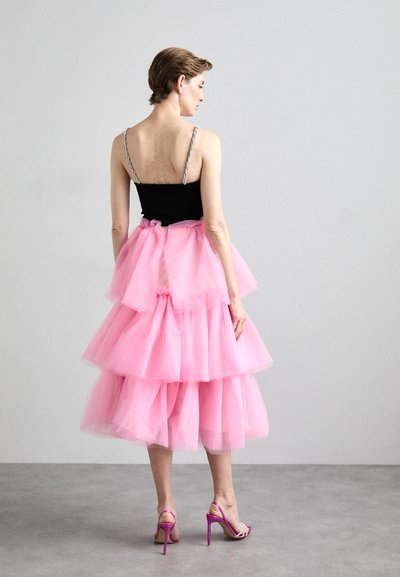 Roze tule jurk met gelaagde, gerimpelde ontwerp. Zwart lijfje met zilveren bandjes; gecombineerd met roze hoge hakken.