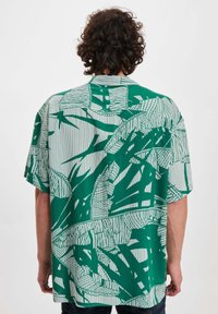 Camicia a maniche corte di colore verde con un motivo astratto di foglie bianche e accenti lineari. Tessuto leggero con vestibilità rilassata e orlo dritto.