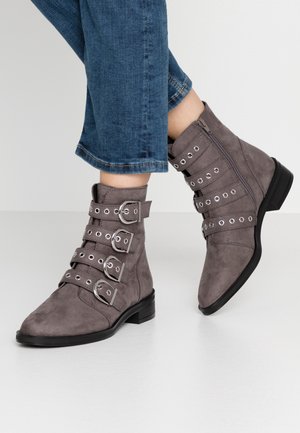 Bottines en suede gris avec quatre sangles décoratives à boucle, quincaillerie argentée, bout pointu et petit talon carré.