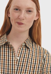 Brown and cream checked shirt with a button-up front and collar. Features a textured fabric with contrasting dark and light checks.
