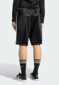 Zwarte fluwelen sportshorts met een relaxte pasvorm, voorzien van witte zijkanten en een elastische tailleband. Gepaard met zwart-witte gestreepte sokken.