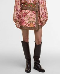Mini-jupe rose courte avec un motif floral dans des tons de vert et de rose, ornée d'une ceinture verte décorative et d'une finition en dentelle ; associée à des bottes marron montantes.