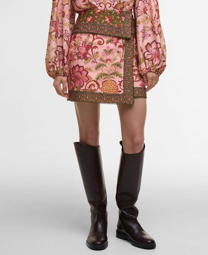 Mini-jupe rose courte avec un motif floral dans des tons de vert et de rose, ornée d'une ceinture verte décorative et d'une finition en dentelle ; associée à des bottes marron montantes.