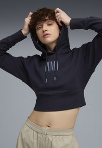 Marineblå cropped hoodie med snore og broderet logo. Har en blød tekstur og ribbet kant. Matcher med lyse beige bukser med snore.
