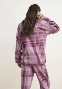 Conjunto de loungewear de felpa rosa con cuadros que incluye una camiseta de manga larga y pantalones holgados, con rayas en diferentes tonalidades de púrpura y un corte relajado.