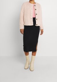 Lyserød blød jakke med rund halsudskæring og fem store knapper, kombineret med en sort midinederdel med sideslidser og beige ankelstøvler.