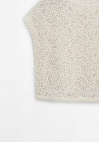 Haut blanc à manches courtes en dentelle avec des motifs floraux et circulaires complexes sur un fond uni.
