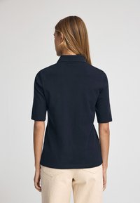 Granatowa koszulka polo z kołnierzykiem, krótkimi rękawami i prostym wykończeniem. Wykonana z gładkiego materiału, ma jednolity wzór bez widocznych deseni.