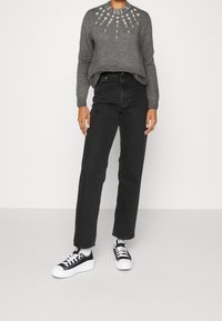 Maglione grigio lavorato a maglia con scollatura decorata, jeans neri a vita alta e sneakers nere con suola e lacci bianchi.