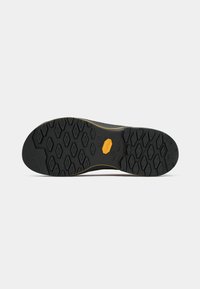 Podplat s črnimi gumijastimi vzorci v obliki diamanta in oranžnim logotipom Vibram na sredini, postavljen na navadno belo ozadje.