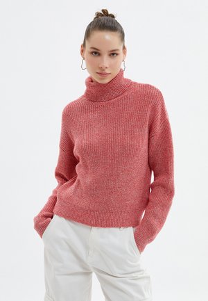 Pull en maille rouge, épais, avec un col roulé haut et des manches longues. Le tissu a une apparence texturée, offrant un look confortable.