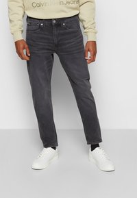 Jeans grises de corte ajustado, con cinco bolsillos, herrajes de metal y una suave textura de denim. Combinados con zapatillas blancas.