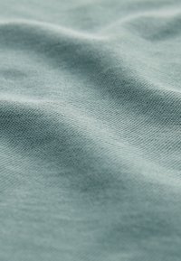 Weiches, strukturiertes Gewebe in einem sanften Teal-Ton, mit einem feinen, subtilen Gewebe und sanftem Fall, das seine glatte, taktile Qualität betont.