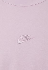 Ljust lila tyg med en liten broderad Nike-logotyp och swoosh i matchande lila tråd nära halsringningen.