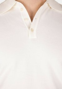 Polo bianco, in cotone finemente lavorato, con colletto classico, pattina con tre bottoni e una sottile texture, dal taglio leggermente rilassato.