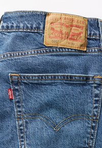 Sinised teksapüksid, millel on pruun nahklabel, millel on tekst ja graafika. Teksad on sinised, nähtav õmblemine ja tagakotil on punane Levi'si silt.
