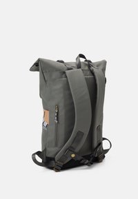 Grauer Rolltop-Rucksack mit verstellbaren Trägern, seitlichem Reißverschlussfach und einem Lederakzent. Hergestellt aus strapazierfähigem Stoff mit einer strukturierten Oberfläche.